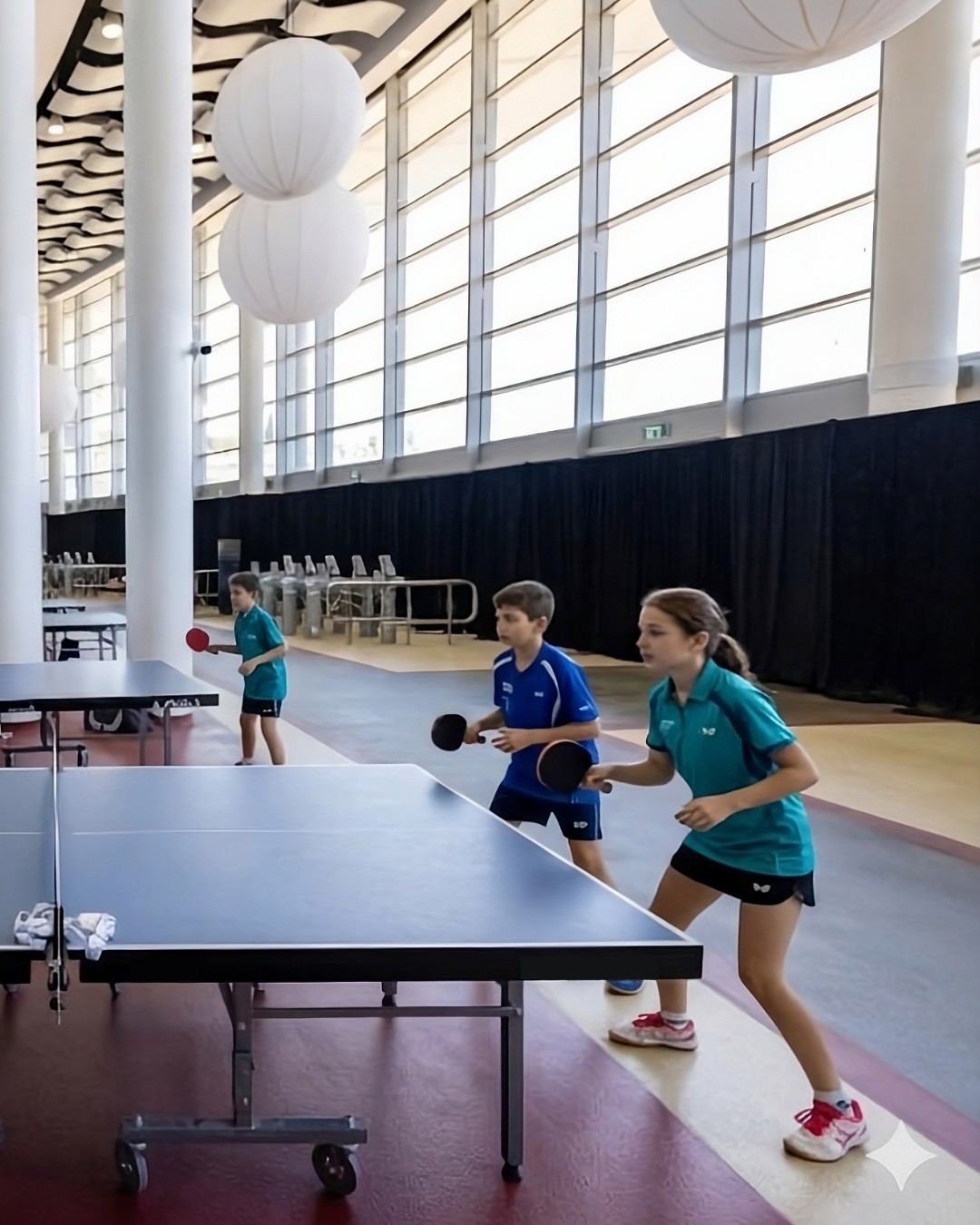 Jugadores de distintas edades jugando tenis de mesa en un amplio vestíbulo iluminado
